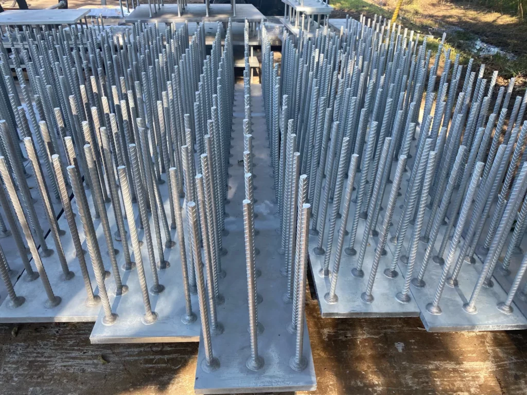 Rows of galvanized threaded anchor bolts standing in template plates outdoors.