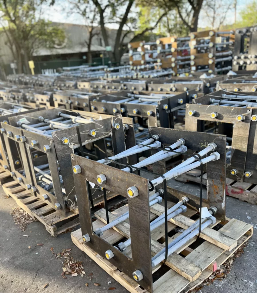 Rows of galvanized steel embed plates with welded channel brackets staged on pallets.