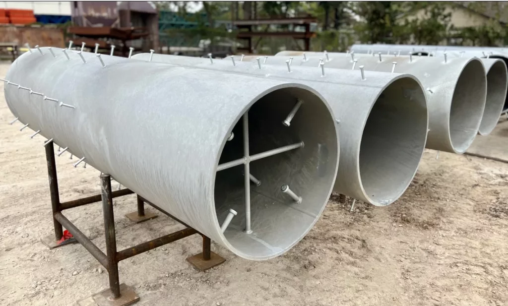 Large galvanized cylindrical pipe embeds with welded shear studs staged in the Madden Bolt yard