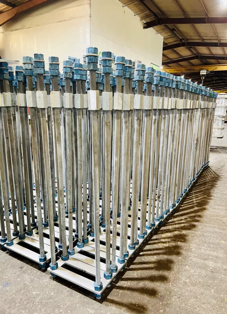 Galvanized anchor bolt sets with heavy hex nuts and square plate washers staged in racks in the shop.