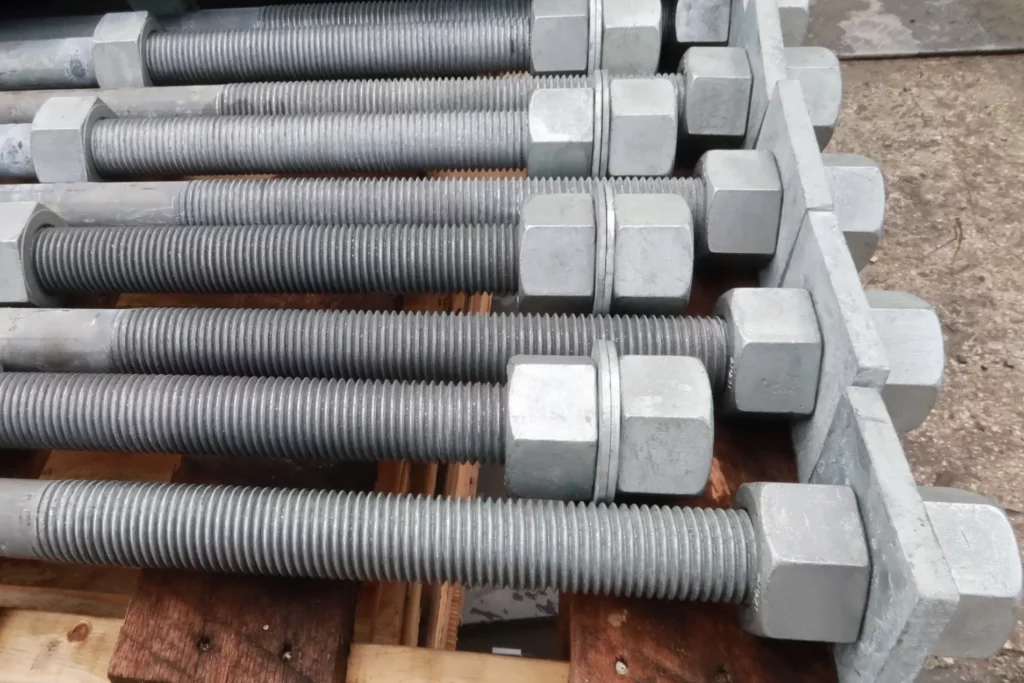 Large-diameter galvanized anchor bolts fitted with heavy hex nuts, staged on a pallet