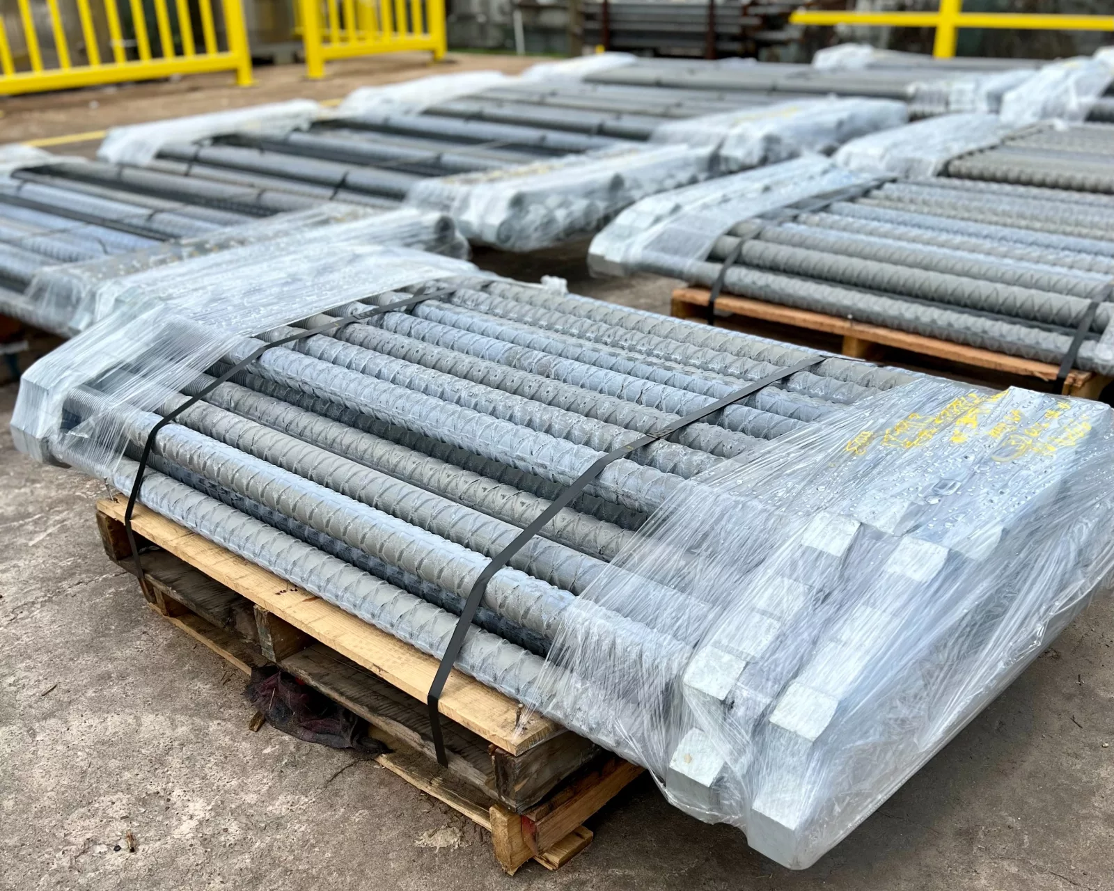 Pallets of wrapped hot-dip galvanized threaded rebar in the yard.