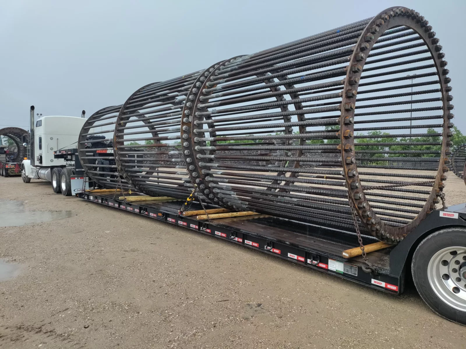 Three large cylindrical rebar anchor cages staged on a flatbed trailer.