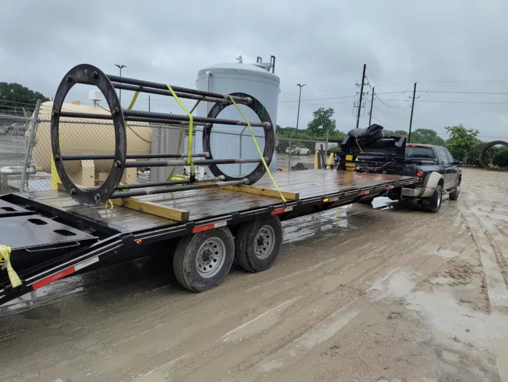 Two rebar anchor ring cages strapped to a gooseneck trailer behind a pickup truck.