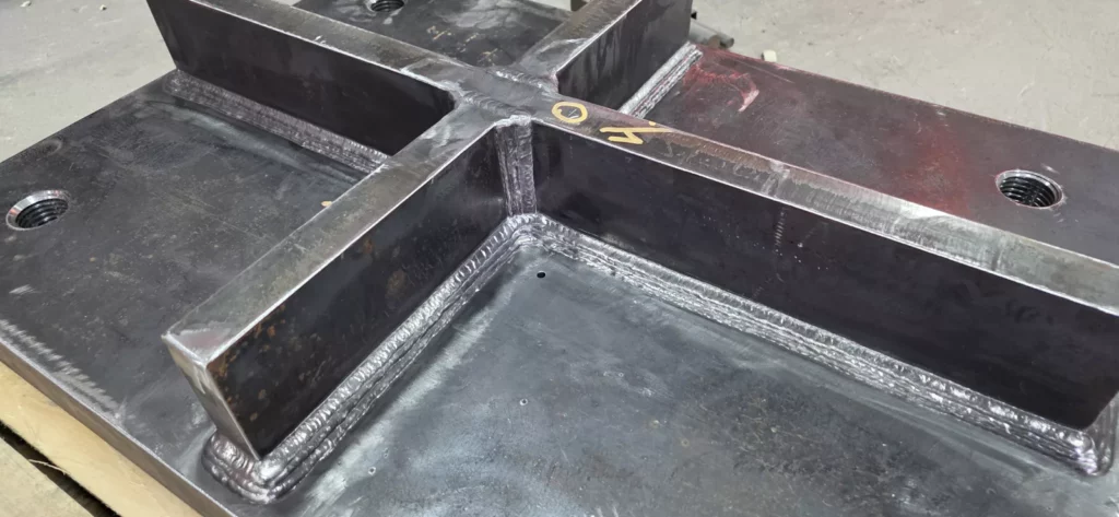 Freshly welded steel embed assembly with stiffener plates in the Madden Bolt fabrication shop